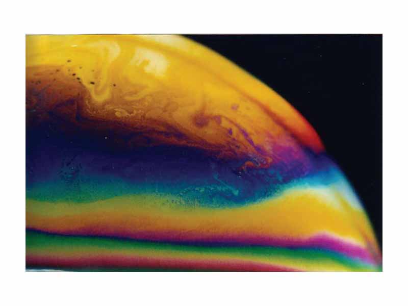 Thin film interference in a soap bubble. Notice the golden yellow colour near the top where the film is thin and a few even thinner black spots.